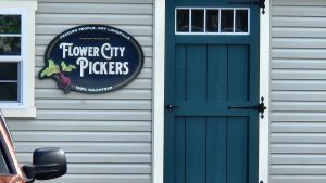 Flower City Pickers sign hanging next to a dark teal door on a gray-sided building.