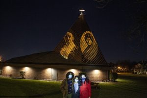 Professor Jasna Bogdanovska and two MCC students standing in front of the Memorial A.M.E. Zion Church with projected images of Hester Jeffrey and Susan B. Anthony.