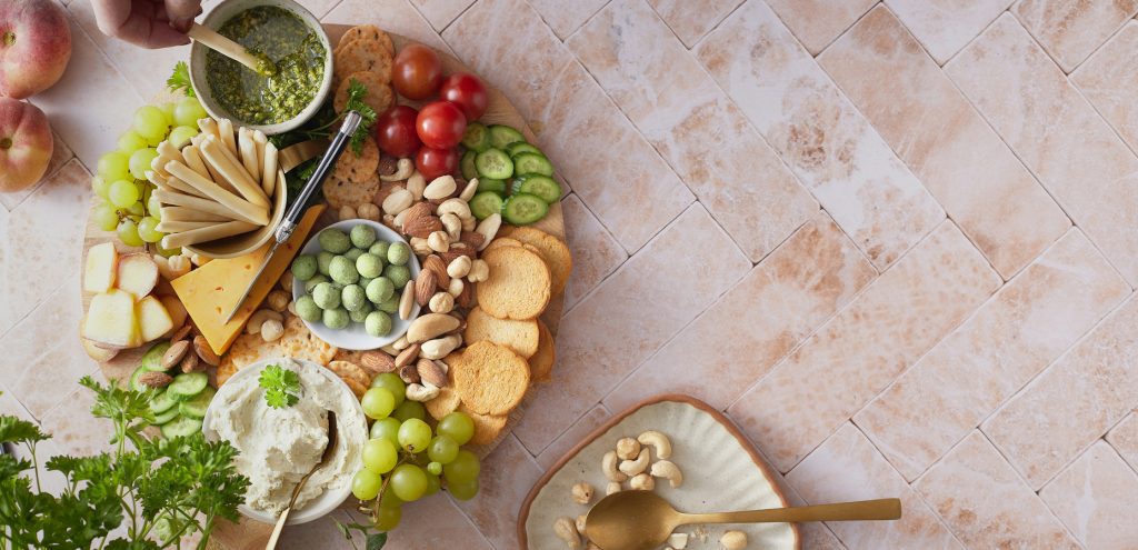 Charcuterie Board with fruit, cheeses, crackers, nuts and spreads along with a plate of food.