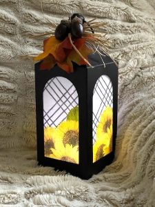 Black and white metal lantern lit up with sunflowers in the window and a netting bow at the top of the lantern
