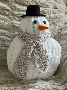 White knit snowman with a black hat, beige scarf and small orange nose.