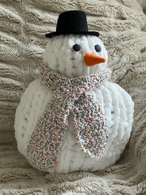 White knit snowman with a black hat, beige scarf and small orange nose.