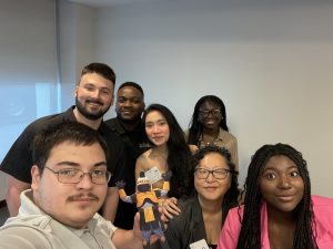 SGA and Presenters with Tiberius –  A group shot of seven people (six students and Dr. Christina Lee) smile at the camera. One student is holding the paper Tiberius.