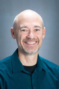 Headshot of Jonathon Little smiling at the camera and wearing a buttoned dress shirt.