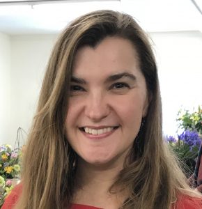 Close-up headshot of April wearing a red shirt with flowers behind her.