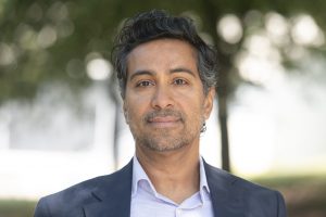 Headshot of Christopher Kumar standing outside wearing a dress shirt and sport jacket.