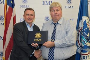 Chuck DiSalvo being presented an award from another male. Chuck is wearing a dress shirt and tie and shaking the presenter's hand.