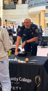 Sam Hillmon standing behind a table, leaning forward to chat with a student during an event. Sam is wearing his uniform and is smiling at the individual.