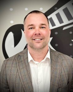 Aaron Bouyea headshot. He is standing in front of the MCC logo and wearing a sport coat.