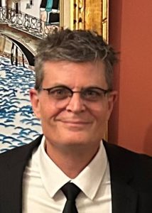 Headshot photo of Dan Raimondo wearing a suit and tie as he smiles at the camera.