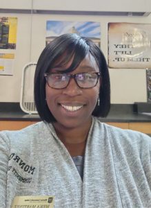 Headshot of Dr. Meka Martinez wearing a gray sweater and glasses.