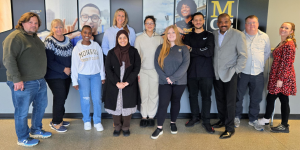 A group photo featuring several members of the Financial Aid Department staff and their student workers, posed in front of an MCC backdrop.
