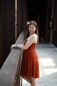 Lauren Feldman wearing an orange dress and standing next to a railing while smiling at the camera.