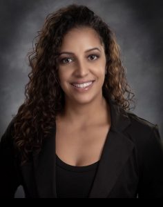 Professional headshot of Michelle Genao wearing a black shirt and blazer on a dark gray background.