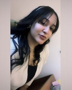 Shacerie has long, dark hair and is wearing a white sweater over a black top.