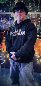Sean Scanlon dressed in denim, a black sweatshirt, black hat, and sunglasses.
