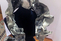 A sculpture of an Elizabethan collar and a face mask both supported by a black sewing manikin. Both the collar and mask are the color of melting snow on the roadside (marbleized grays, browns, and white). The collar is ruffled in the style of queen Elizabeth. The entire outfit is made of paint that after being allowed to dry in flat pools, was peeled up and then sewn into these forms. (Right View)