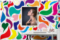 A photographi image of a desk in a room, and on the wall in the center of the image hangs a photo of a woman  in profile. The wall is covered with abstract shapes in various bright colors.
