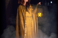 A photograph of a young girl dressed in flowing golden robes is is standing in front of a tree at night, a lamp is in her left hand and fog is billowing around her legs.