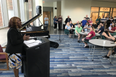 This image shows a group of people sitting at tables on the right, listening to MCC President Dr. Deanna Burt-Nanna speaking during the award ceremony.