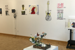This is a photograph of the 44th annual student art exhibition installation. In this image we are seeing a small section of the right wall of the gallery with 12 pieces of art installed in the space.
