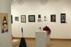 This is a photograph of the 44th annual student art exhibition installation. In this image we are seeing a small section of the rear wall of the gallery with 14 pieces of art installed in the space.