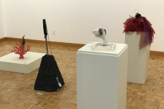 This is a photograph of the 44th annual student art exhibition installation. In this image we are seeing a small section of the floor near the rear of the gallery with 4 pieces of art on pedestals installed in the space.