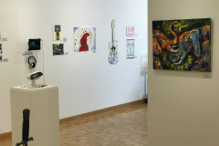 This is a photograph of the 44th annual student art exhibition installation. In this image we are seeing a small section of the right wall of the gallery with 9 pieces of art installed in the space.
