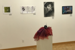 This is a photograph of the 44th annual student art exhibition installation. In this image we are seeing a small section of the right wall of the gallery with 5 pieces of art installed in the space.