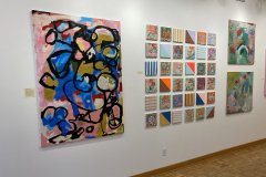 Exhibition installation view showing one large painting next to thirty six small paintings in a grid.