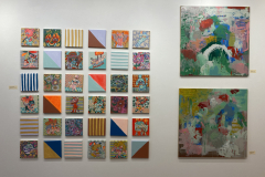 Exhibition installation showing thirty six small paintings in a grid next to two larger paintings.