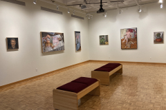 Installation shot of the left side of the gallery, containing six paintings of various sizes and subject matter hanging evenly down the wall.