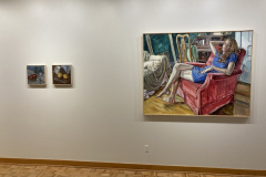Installation shot of exhibition, two small paintings of arranged fruit are hung on the left, and one large painting of a woman is hanging on the right.