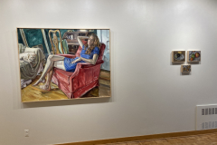 Installation shot of exhibition, three small painting of various fruits and seeds are hung on the right, and one large painting of a woman is hanging on the left.