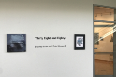 This is a photograph taken outside the gallery showing two art works by the artists and lettering on the wall saying the name of the exhibition. At the right of the image we can see more artwork inside the gallery.