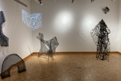 Image showing installation of art in the Mercer Gallery. Abstract forms on the wall and floor, and one hanging frm the ceiling. A video is projected in the corner of the gallery.