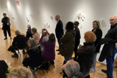 An image showing a group of people in the gallery, listening to the artist speak.
