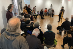 An image showing a group of people in the gallery, listening to the artist speak.