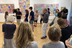 Image of Artist Reception, people watching Claire be interviewed by news station.