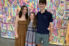 Image showing the artist Claire with her sister and brother in front of one of her colorful drawings.