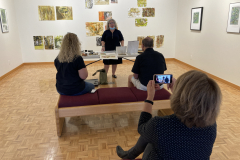 Image of artist giving lecture in gallery, showing examples of how she makes her artwork.