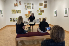 Image of artist giving lecture in gallery, showing examples of how she makes her artwork.