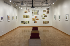 Wide installation shot of gallery, showing arrangement of various prints on rear wall of gallery, and framed prints hung evenly on the right and left walls..