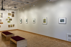 Wide installation shot of gallery back right corner, on the left is the rear wall with prints hung randomly, and on the right wall are five prints framed hung evenly.