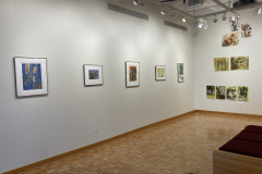 Wide installation shot of gallery back left corner, on the right is the rear wall with prints hung randomly, and on the left wall are five prints framed hung evenly.