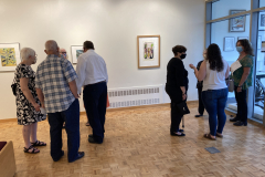 Image from the opening reception, prints are hanging on the walls and a small group of visitors is gathered in various spots around the work.