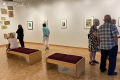 Image from the opening reception, prints are hanging on the walls and a small group of visitors is gathered in various spots around the work.