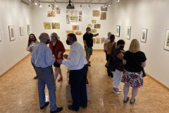 Image from the opening reception, prints are hanging on the walls and a small group of visitors is gathered in various spots around the work.