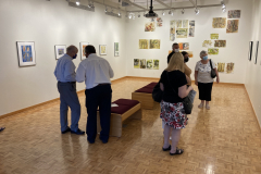 Image from the opening reception, prints are hanging on the walls and a small group of visitors is gathered in various spots around the work.