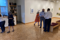 Image from the opening reception, prints are hanging on the walls and a small group of visitors is gathered in various spots around the work.